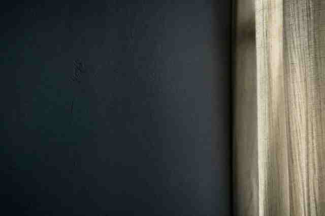A dark wall with a linen curtain at its edge in soft light
